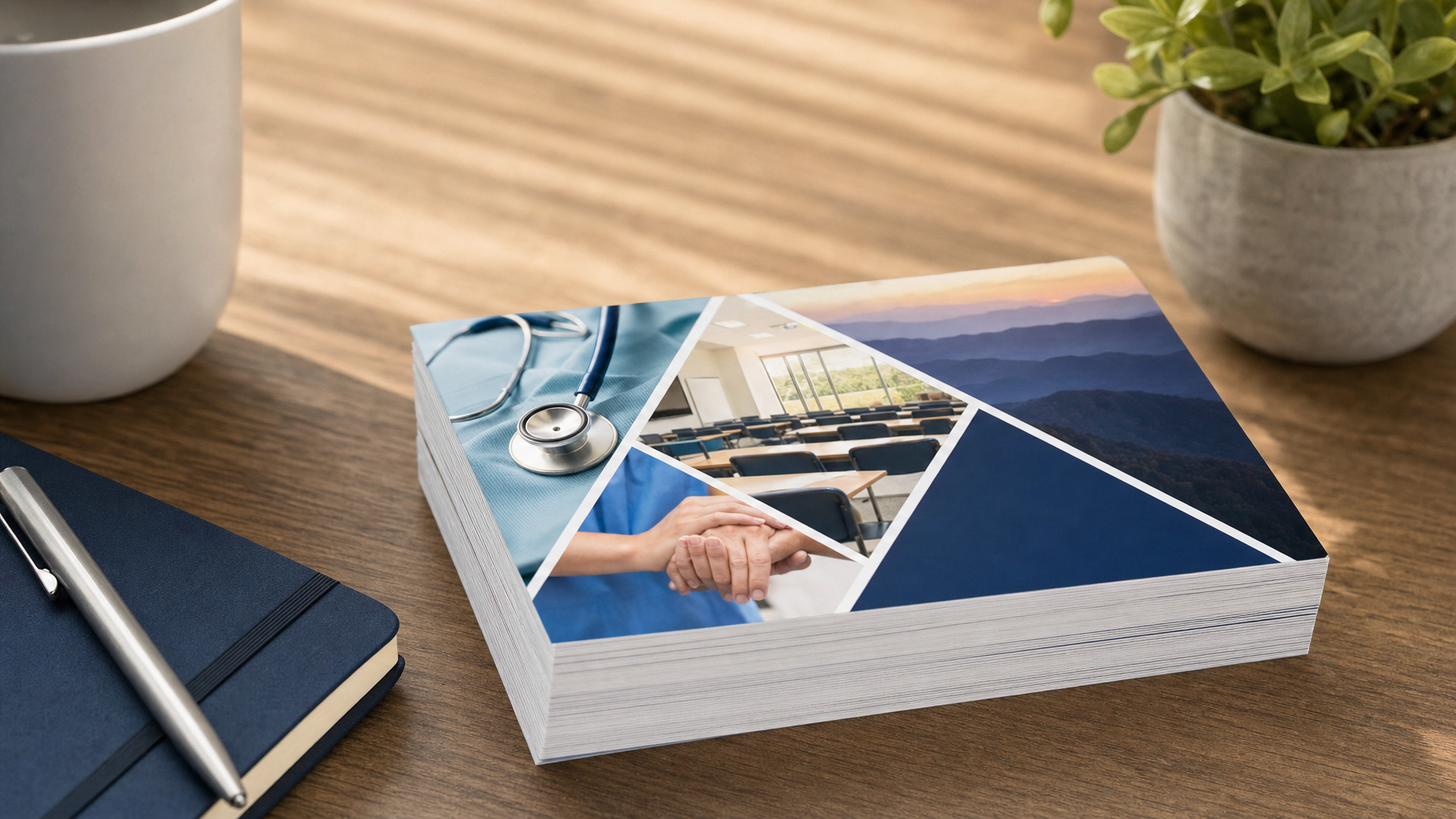 A stack of brochures with a stethoscope, classroom, landscape, and hands on the cover sits on a wooden desk beside a notebook, pen, mug, and potted plant.