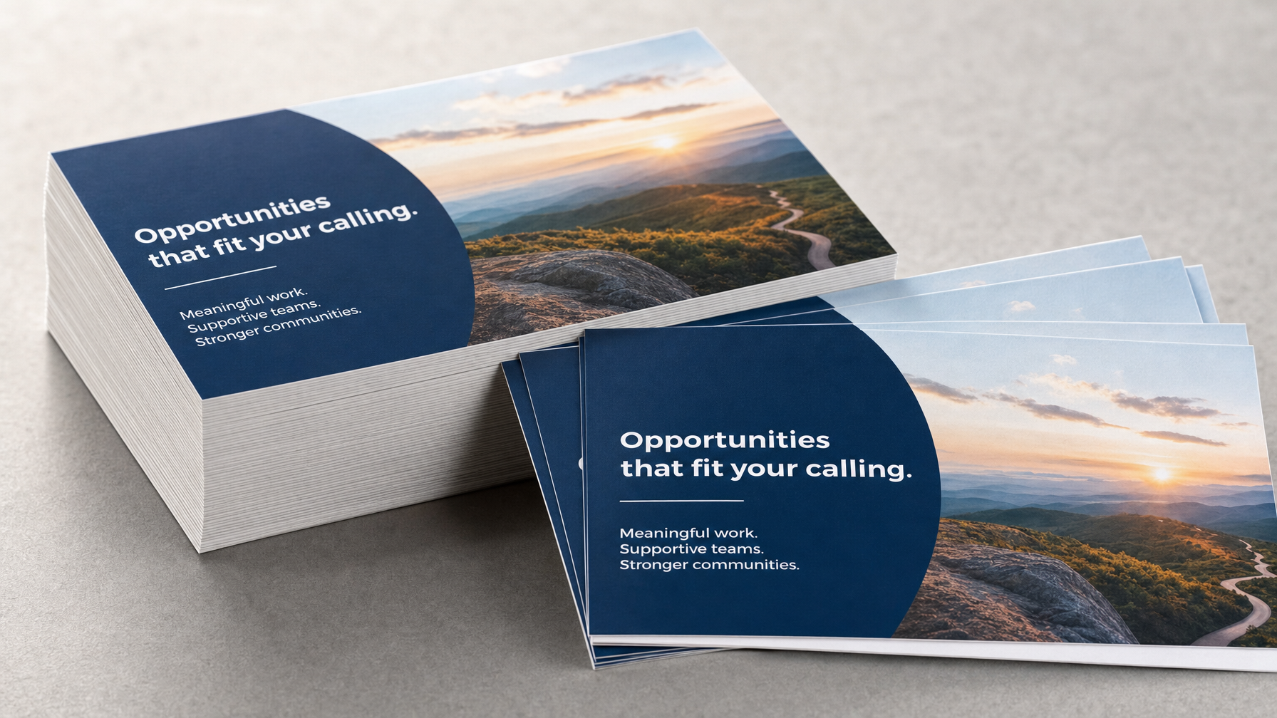 Stacks of postcards with blue text panels and mountain landscape images rest on a gray tabletop, with several loose postcards in the foreground.